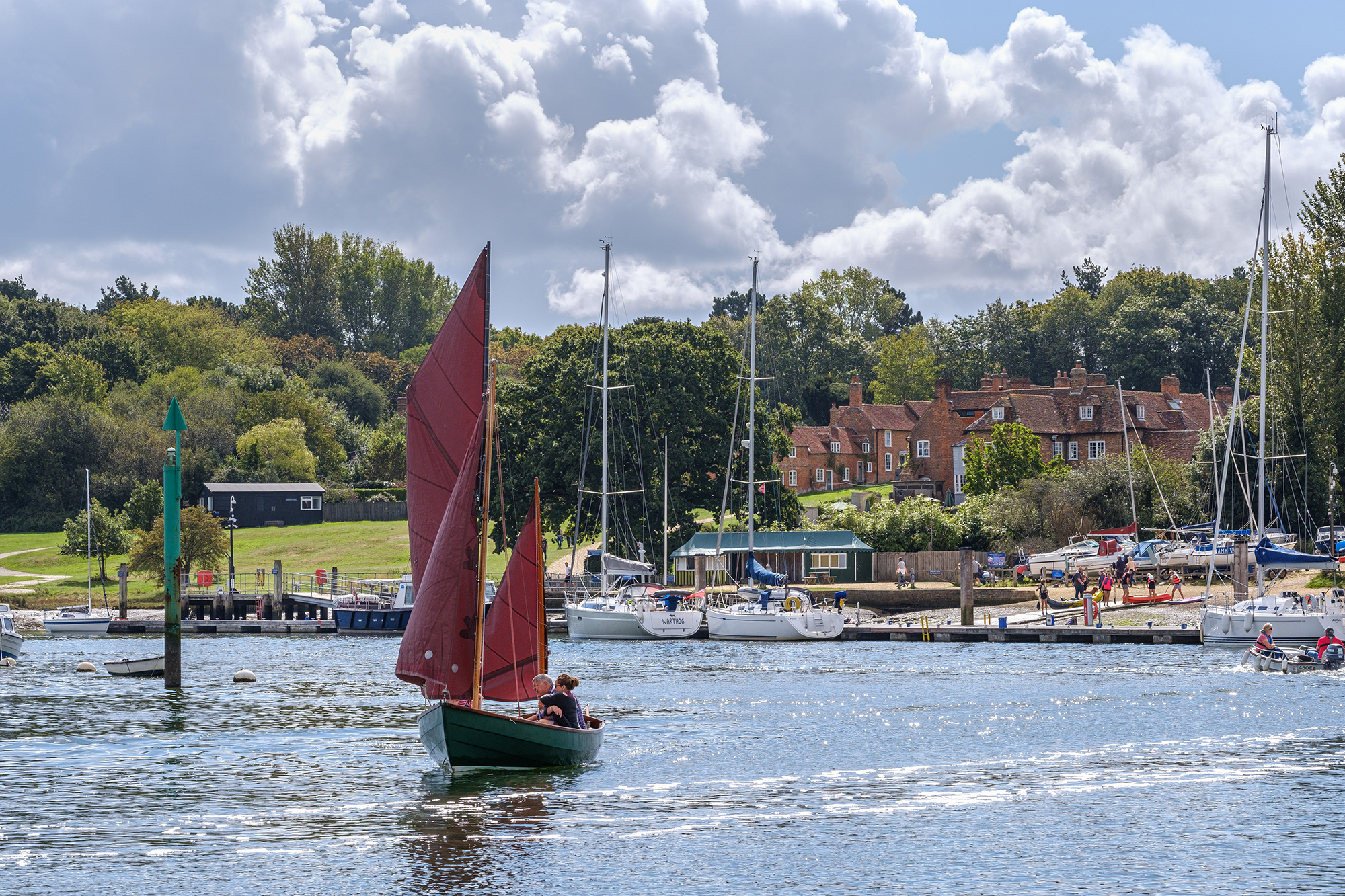 Boat sailing past Buckler's Hard Village on the Beaulieu River